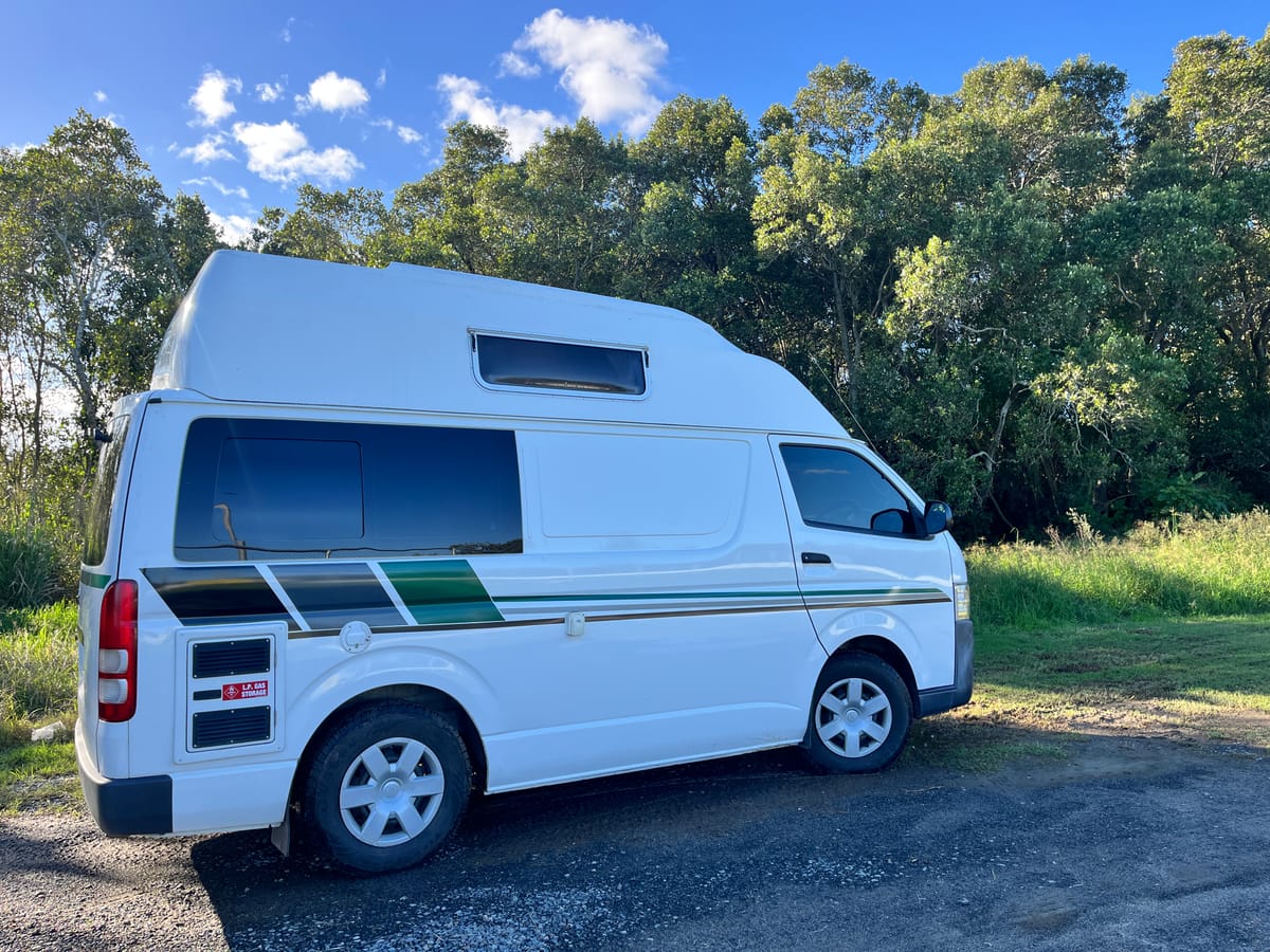 Toyota Hiace hitop camper, side profile under blue sky and trees
