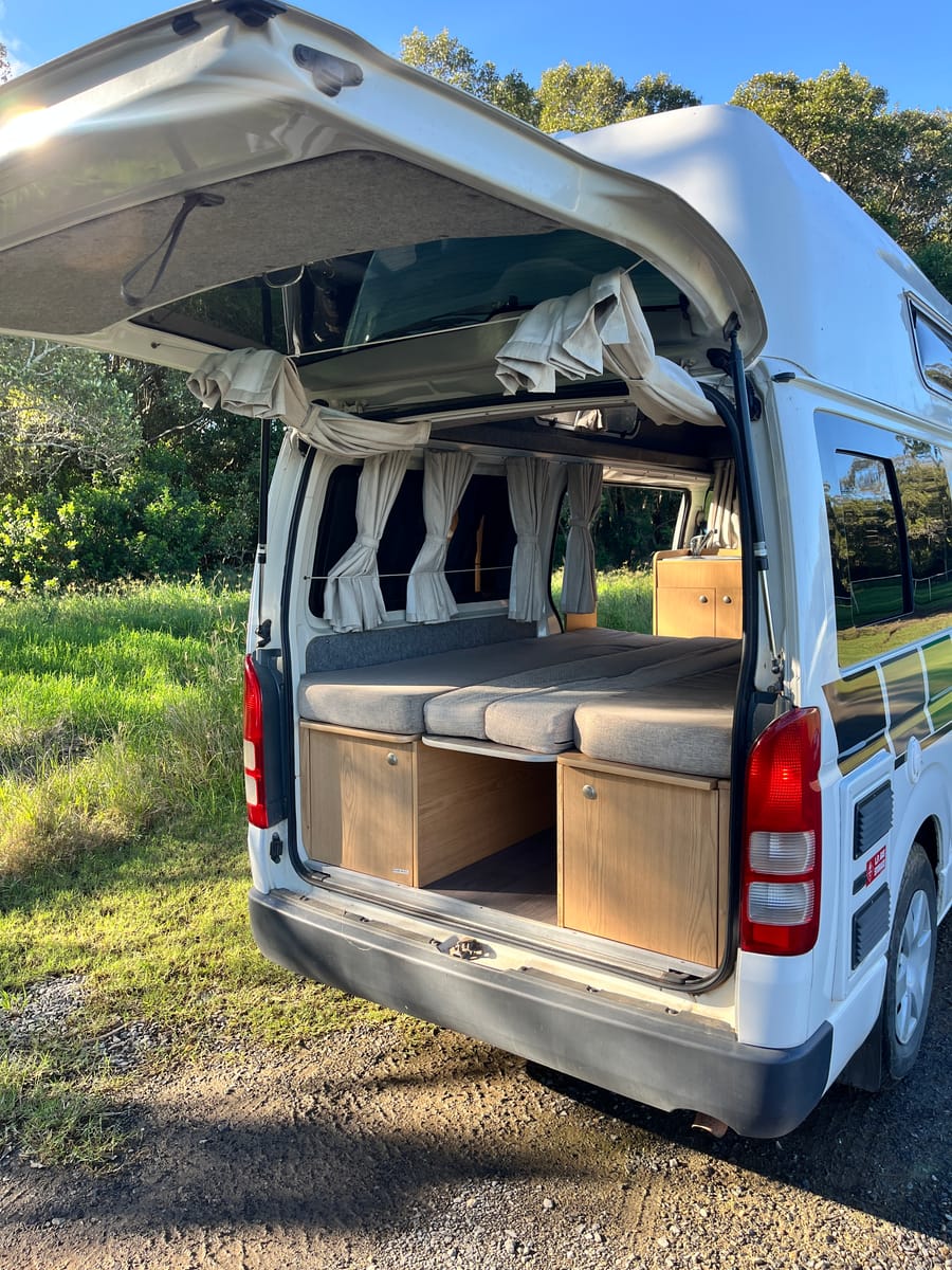 Toyota Hiace hitop camper, rear doors open with comb bed made up, golden hour